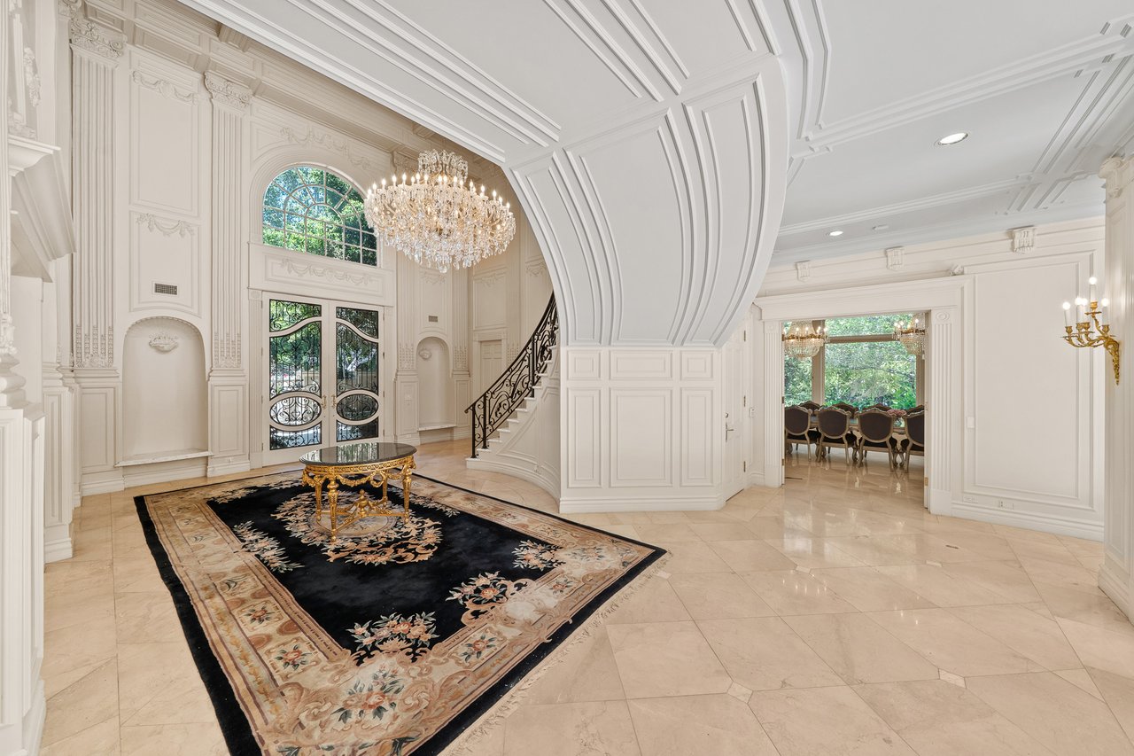 Grand foyer with a crystal chandelier, curved staircase, and arched glass entry doors.