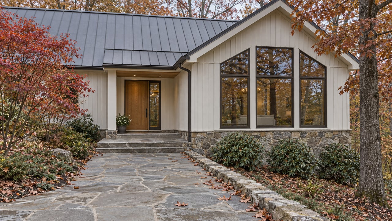 A pale timber home with a stone foundation and oak entry, approached over flagstone beneath red and russet autumn foliage.