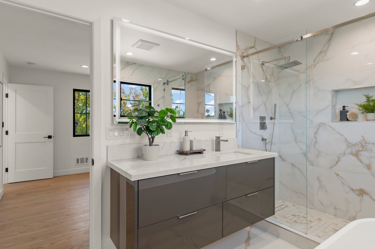 Modern bathroom with a dark floating vanity, large mirror, and glass-enclosed marble-look shower.