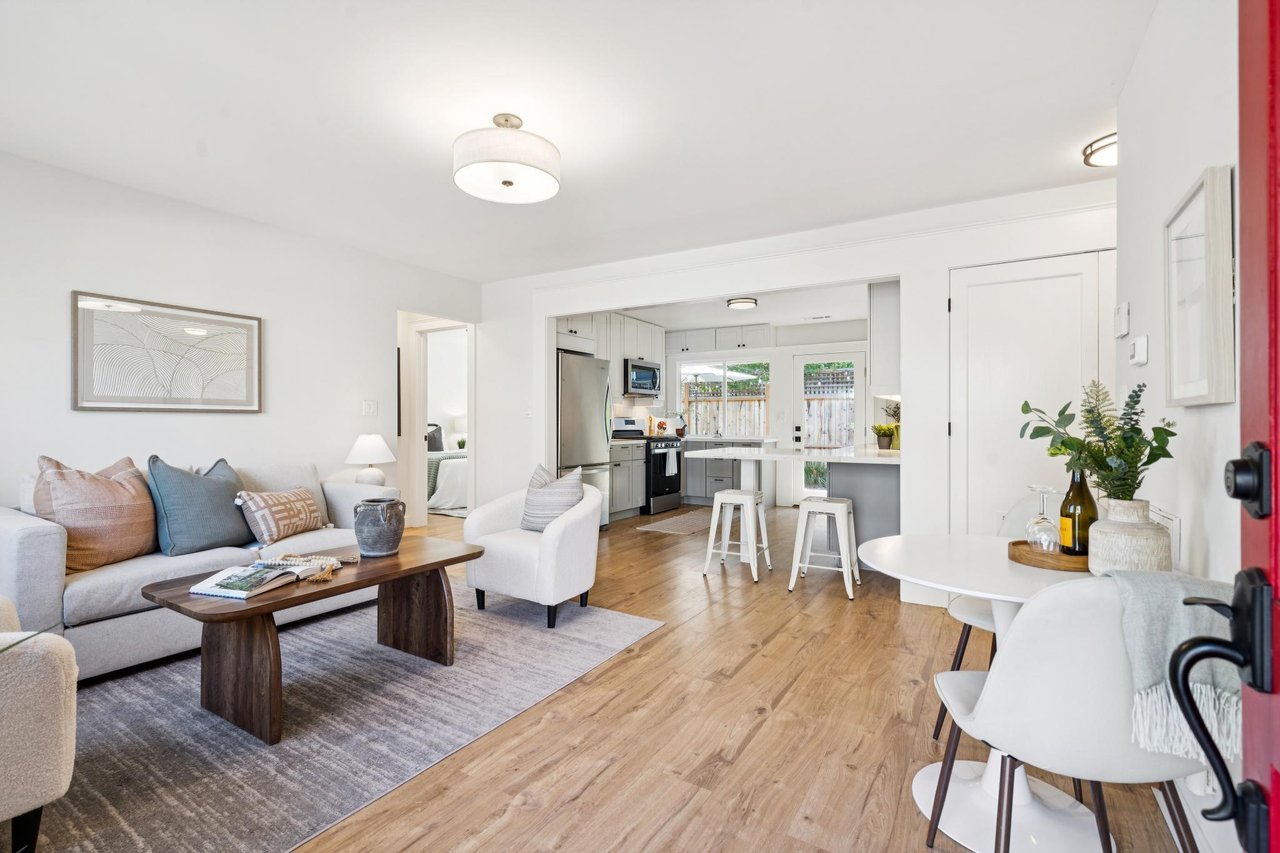 Open-plan living room and kitchen with a gray sofa, wood floors, and island seating.