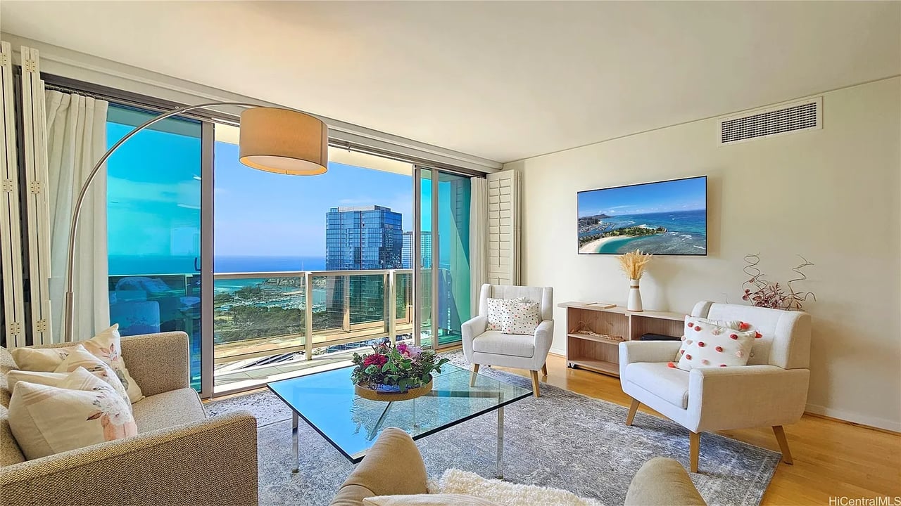 Living room with sliding balcony doors overlooking the ocean and nearby high-rise buildings.