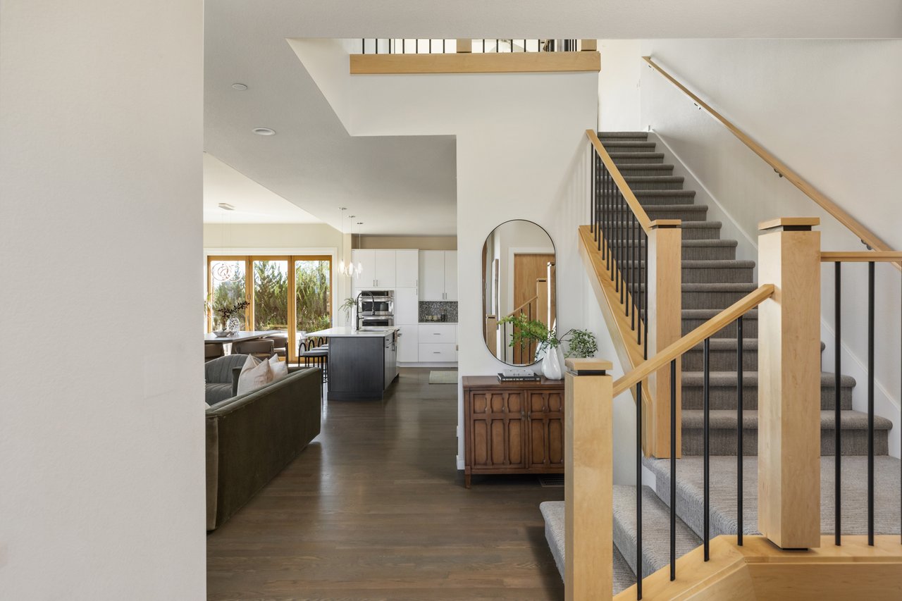 Entry view of the staircase with light wood posts and black balusters, with the living room and kitchen beyond