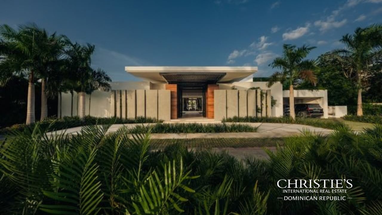 Modern villa with a wood-accented entrance, tropical landscaping, and a vehicle in the carport.