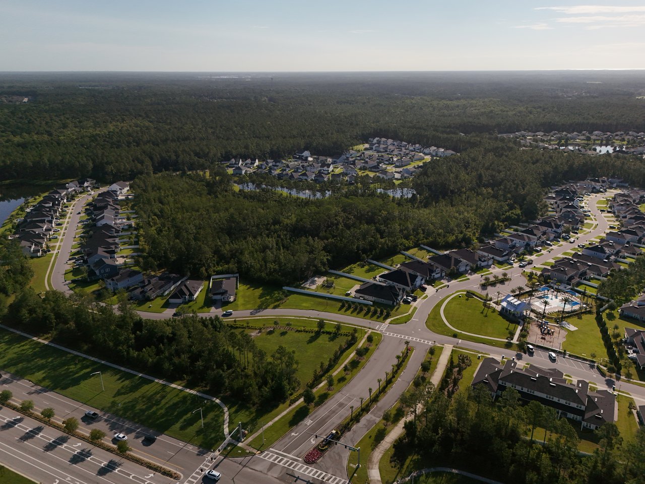 Aerial view of homes and curving streets beside wooded areas, with a neighborhood pool in the foreground.