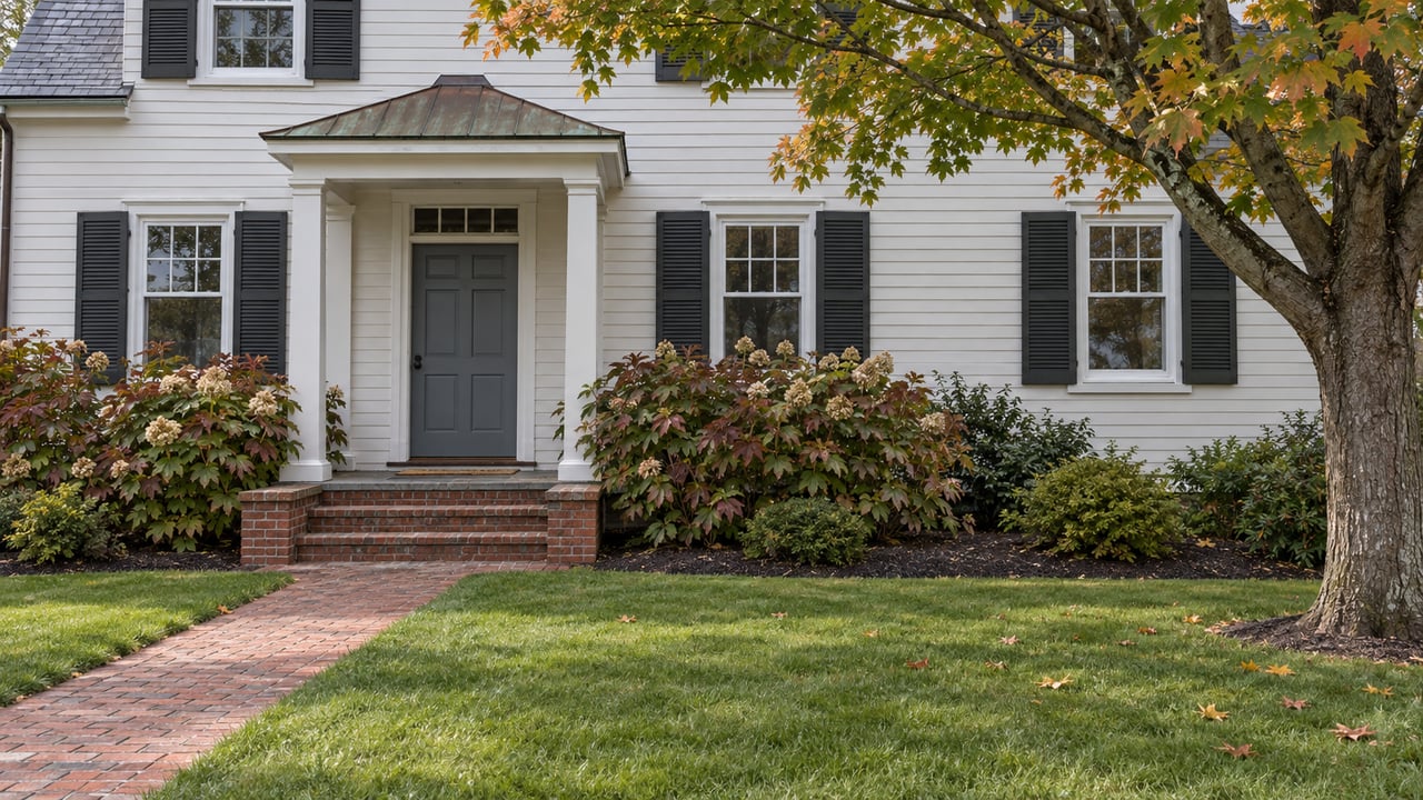 White clapboard home with a blue-gray entry door, copper portico, worn brick steps and an established autumn garden.
