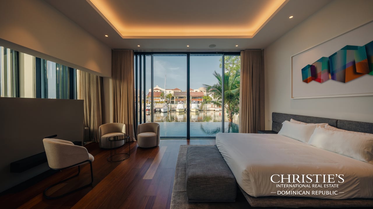 Furnished bedroom with floor-to-ceiling windows overlooking marina water and boats.