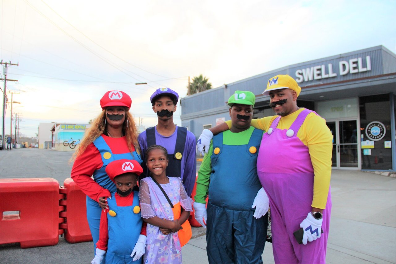 Six people, including two children, pose in Mario and Luigi costumes outside Swell Deli.