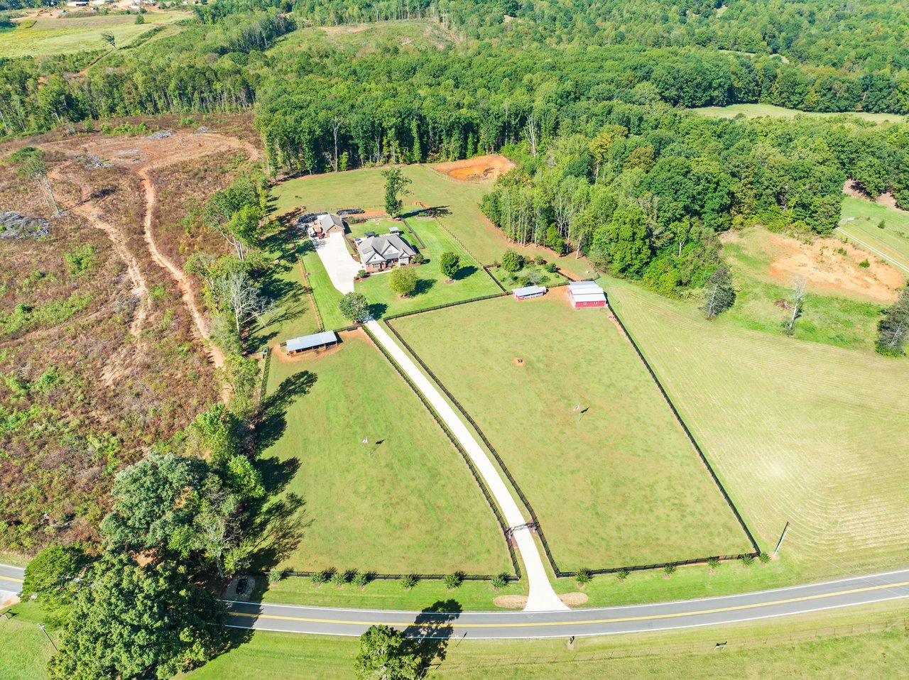 Aerial view of a home, red barns, and fenced pasture surrounded by woods.