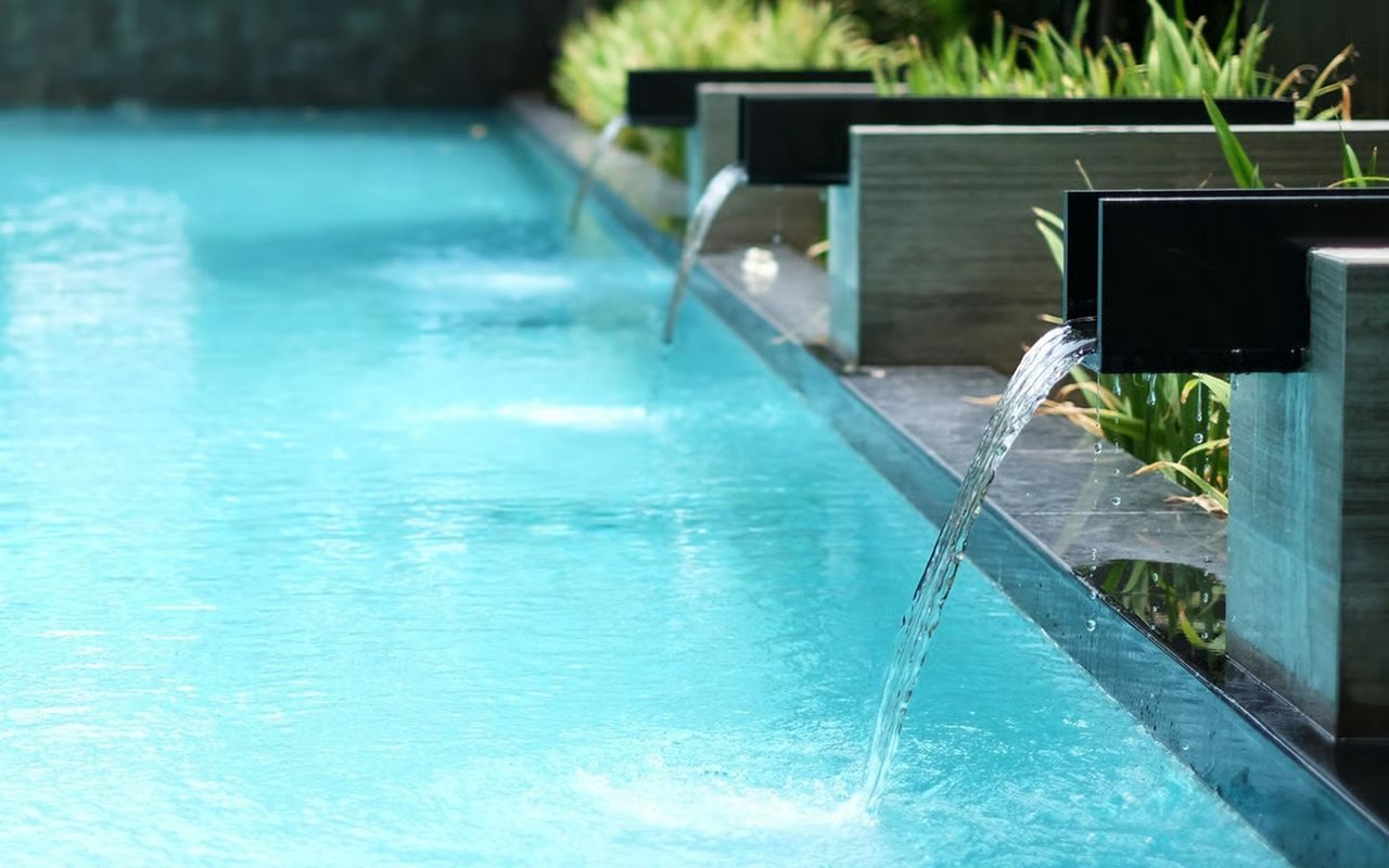 Turquoise pool with water pouring from dark rectangular spouts along its stone edge.