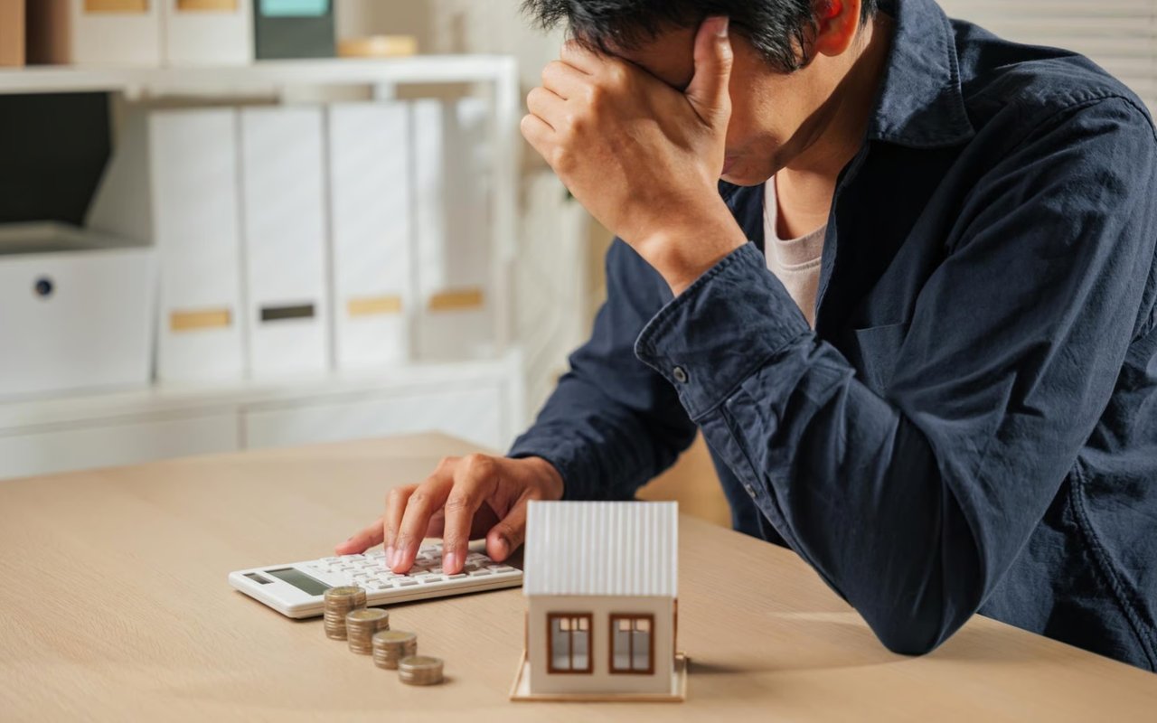Man calculates home costs beside coins and a model house.