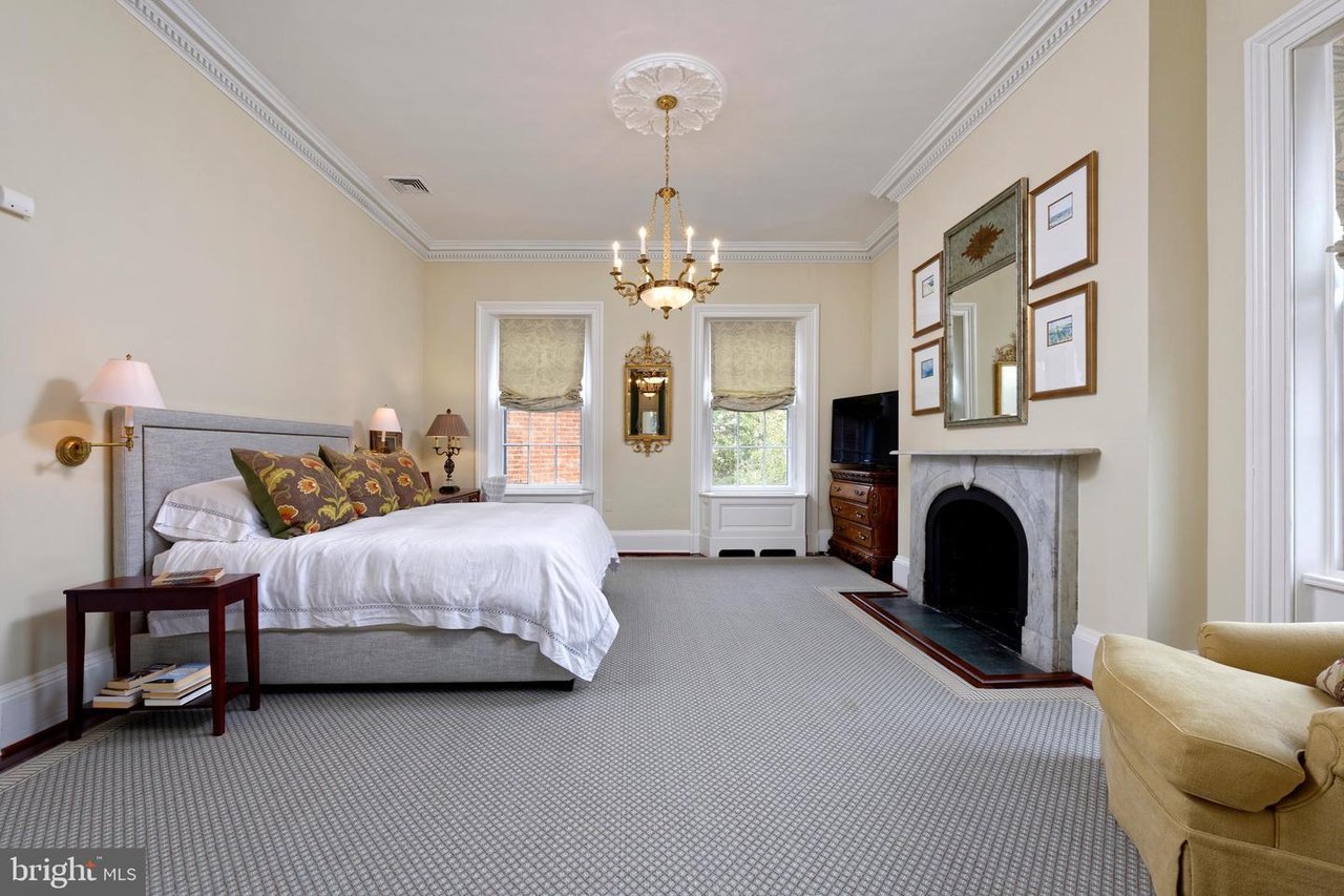 Bedroom with an upholstered bed, tall windows, and a marble fireplace.