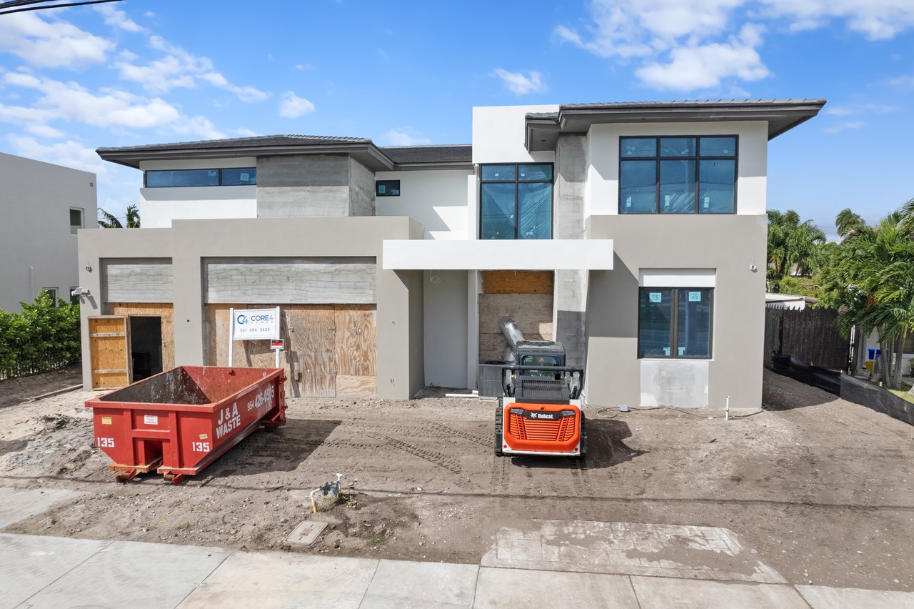 Modern two-story house under construction, with plywood-covered garage openings and construction equipment outside.