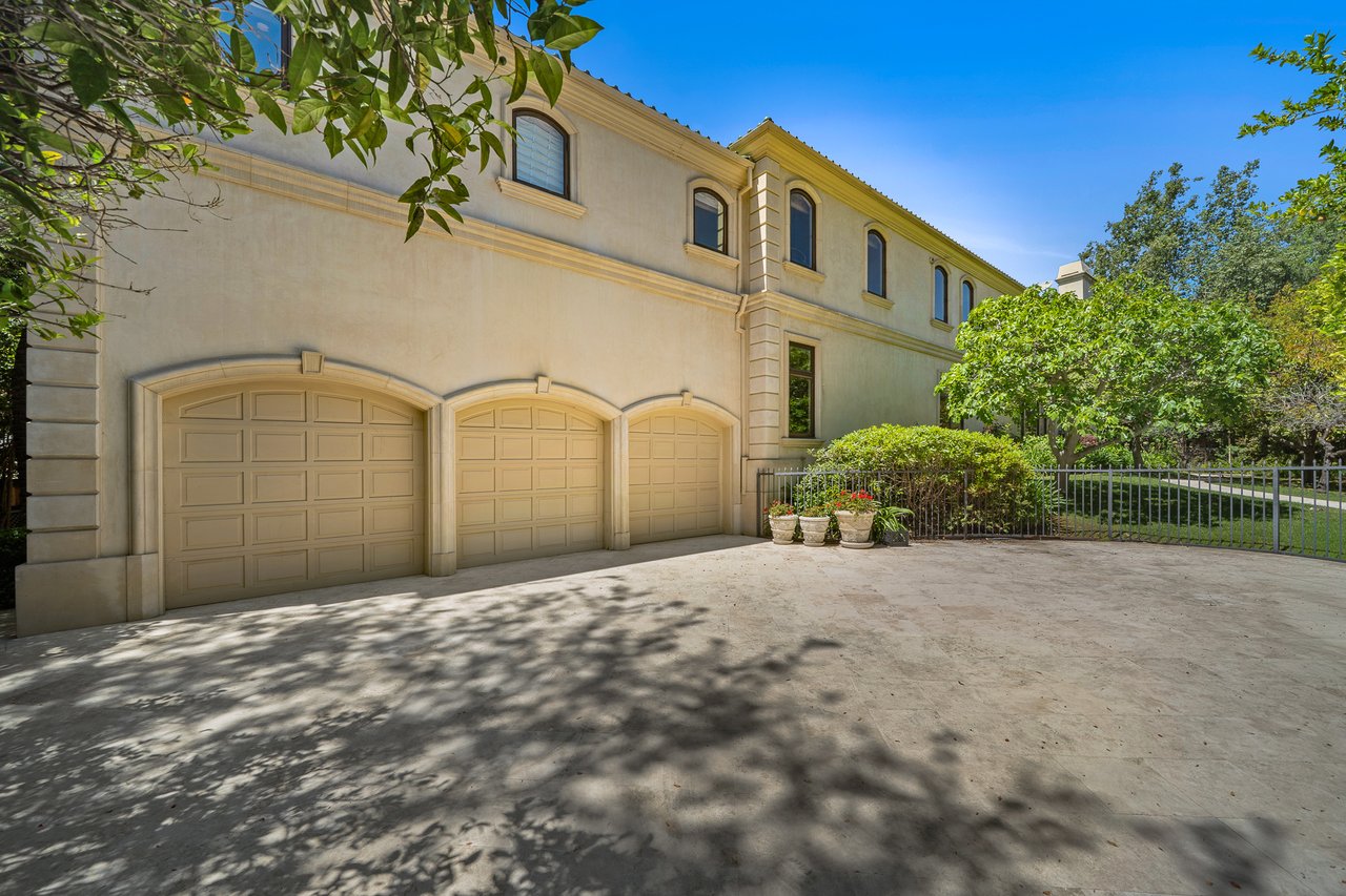 Large beige stucco home with three garage doors and a broad driveway.