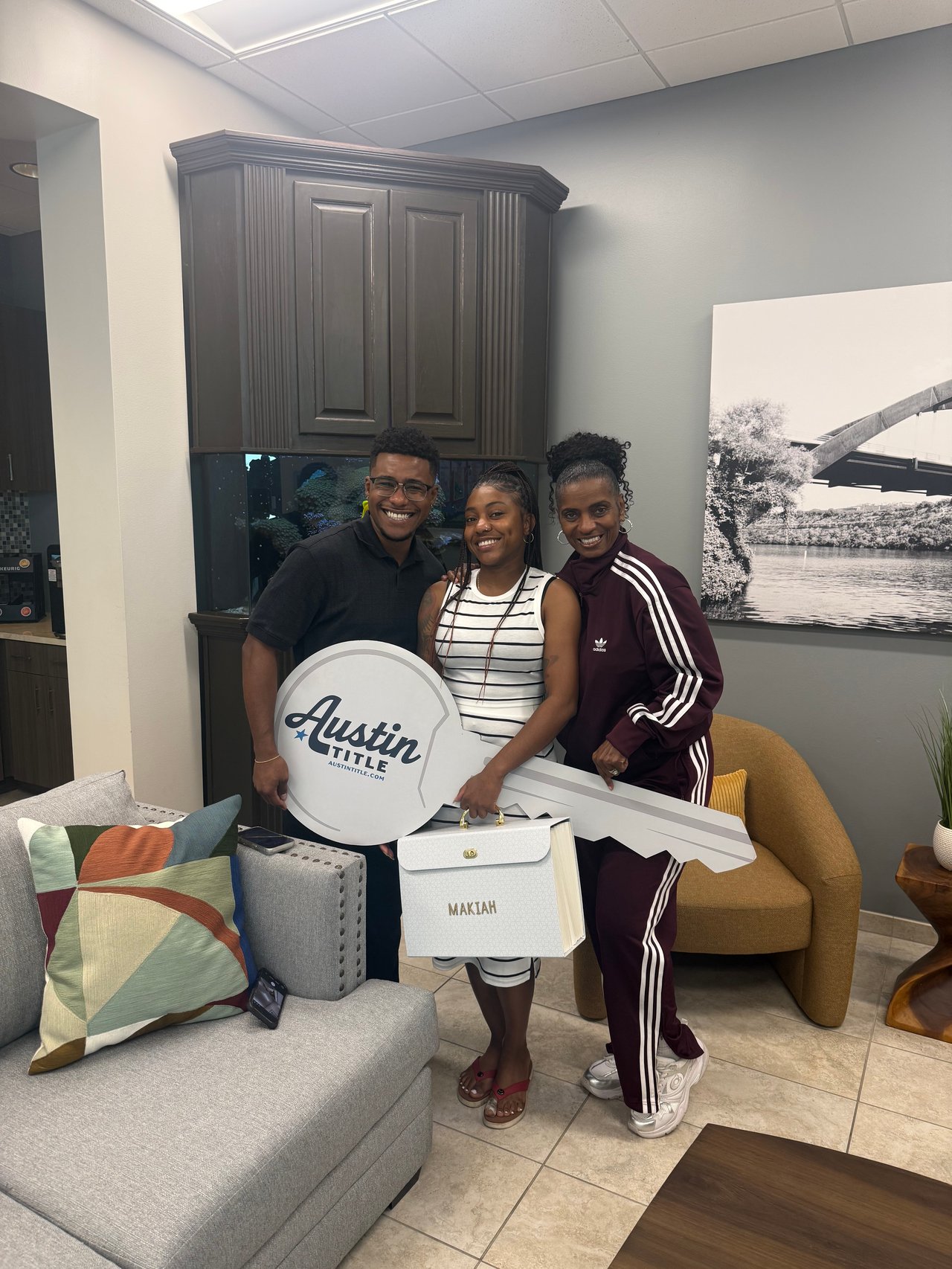 Three smiling people pose with an oversized Austin Title key and a gift bag.
