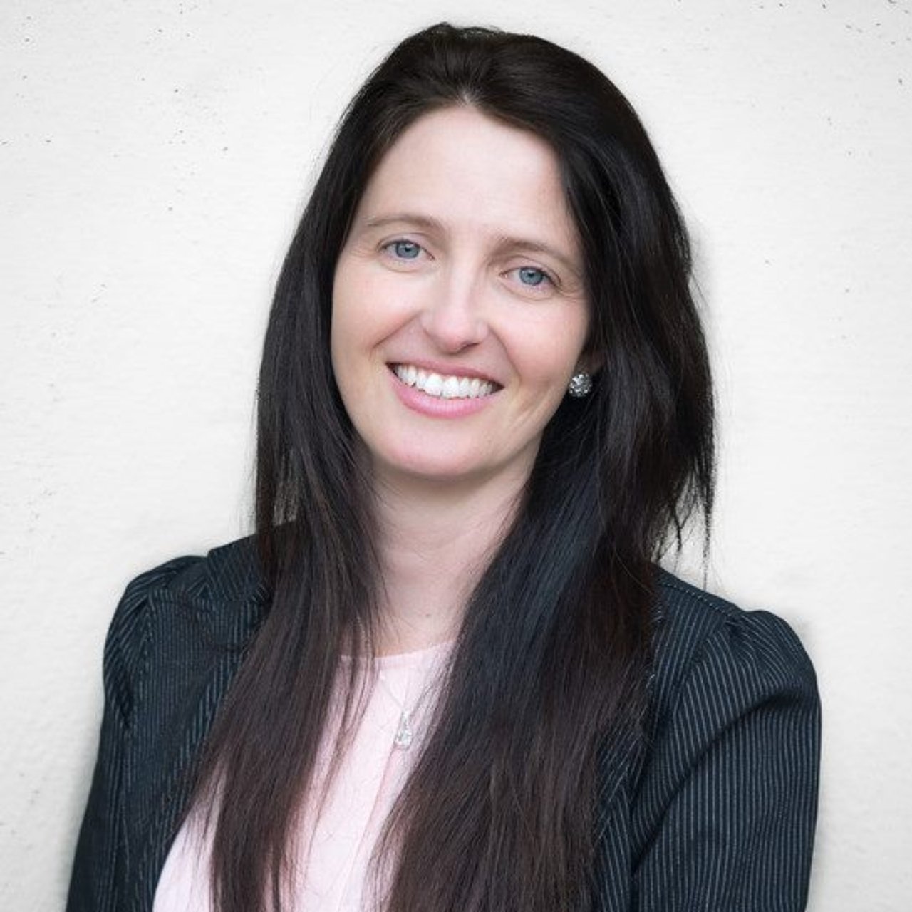 Cristiane Gois smiling in a dark pinstriped blazer.