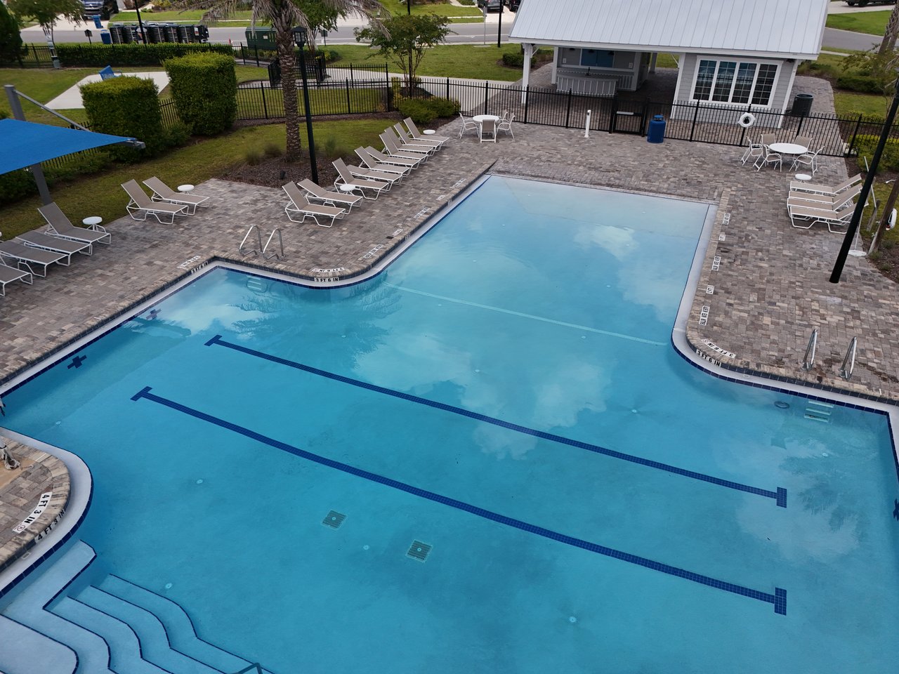 Outdoor pool with lap lanes, curved entry steps, and lounge chairs on a paved deck.