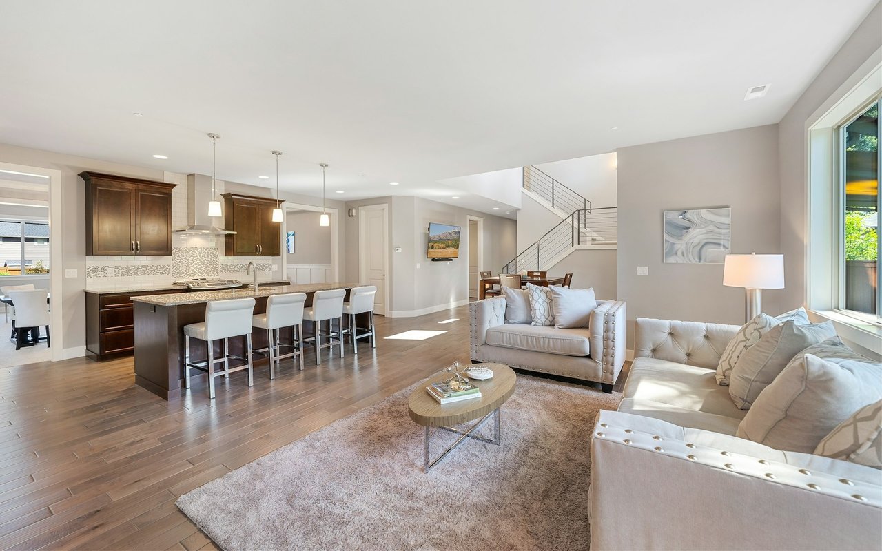 Staged open-plan living room and kitchen with a white sectional, dark wood cabinetry, and island seating.
