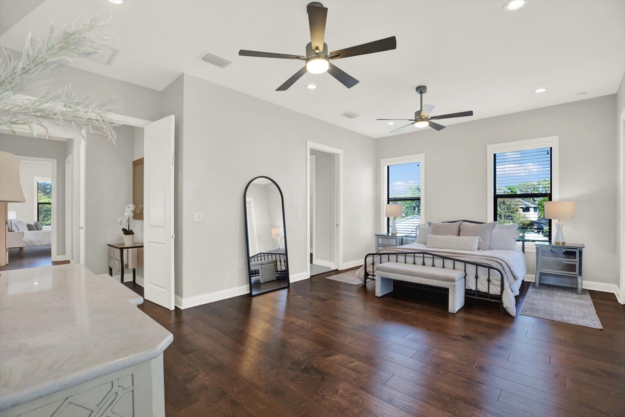Bright staged bedroom with a black metal bed, dark wood floors, and two ceiling fans.