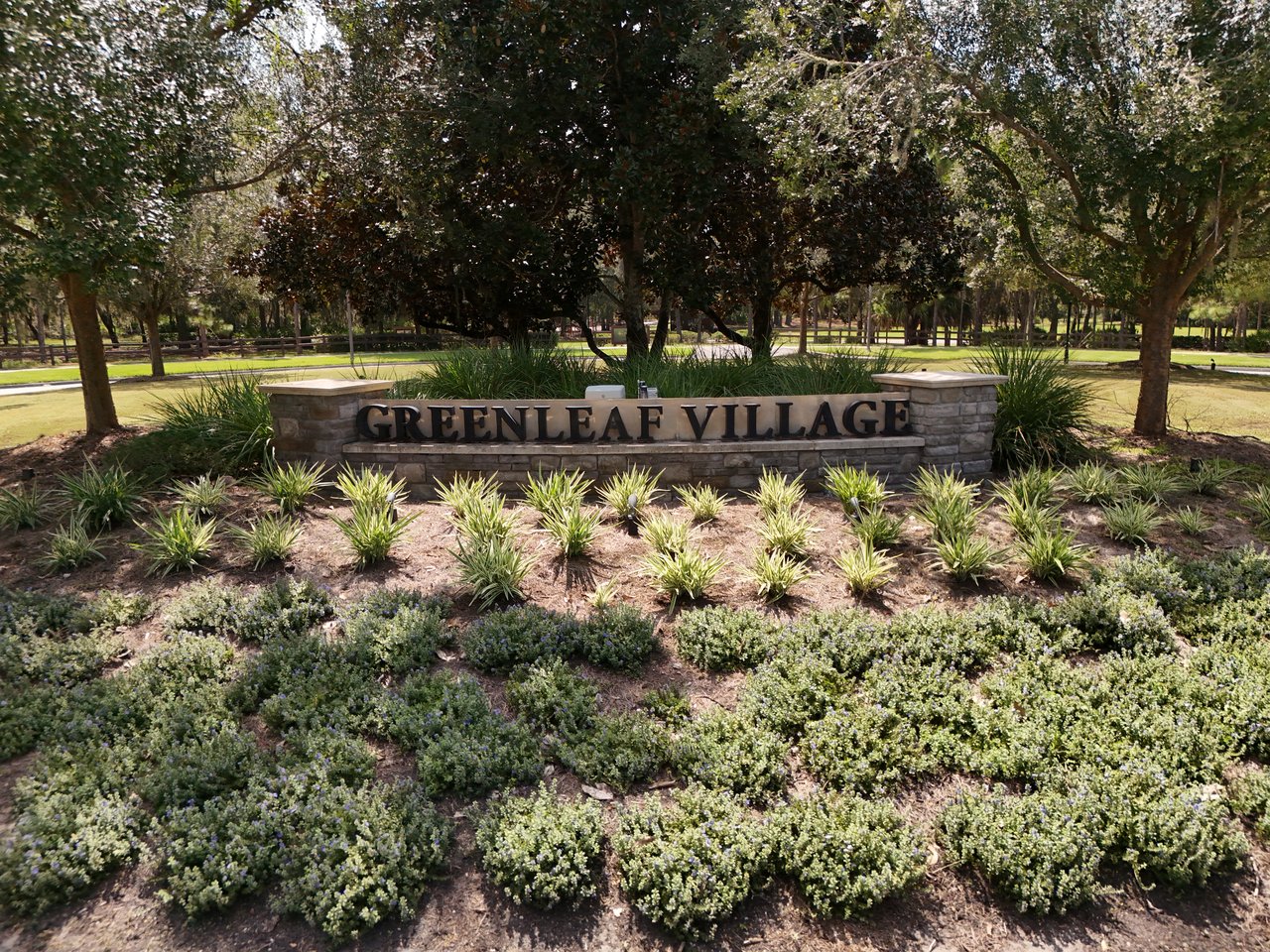 Greenleaf Village entrance sign amid landscaped beds and mature trees.