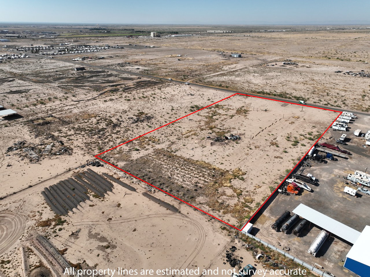 Vacant sandy parcel outlined in red beside a road and commercial equipment yard.