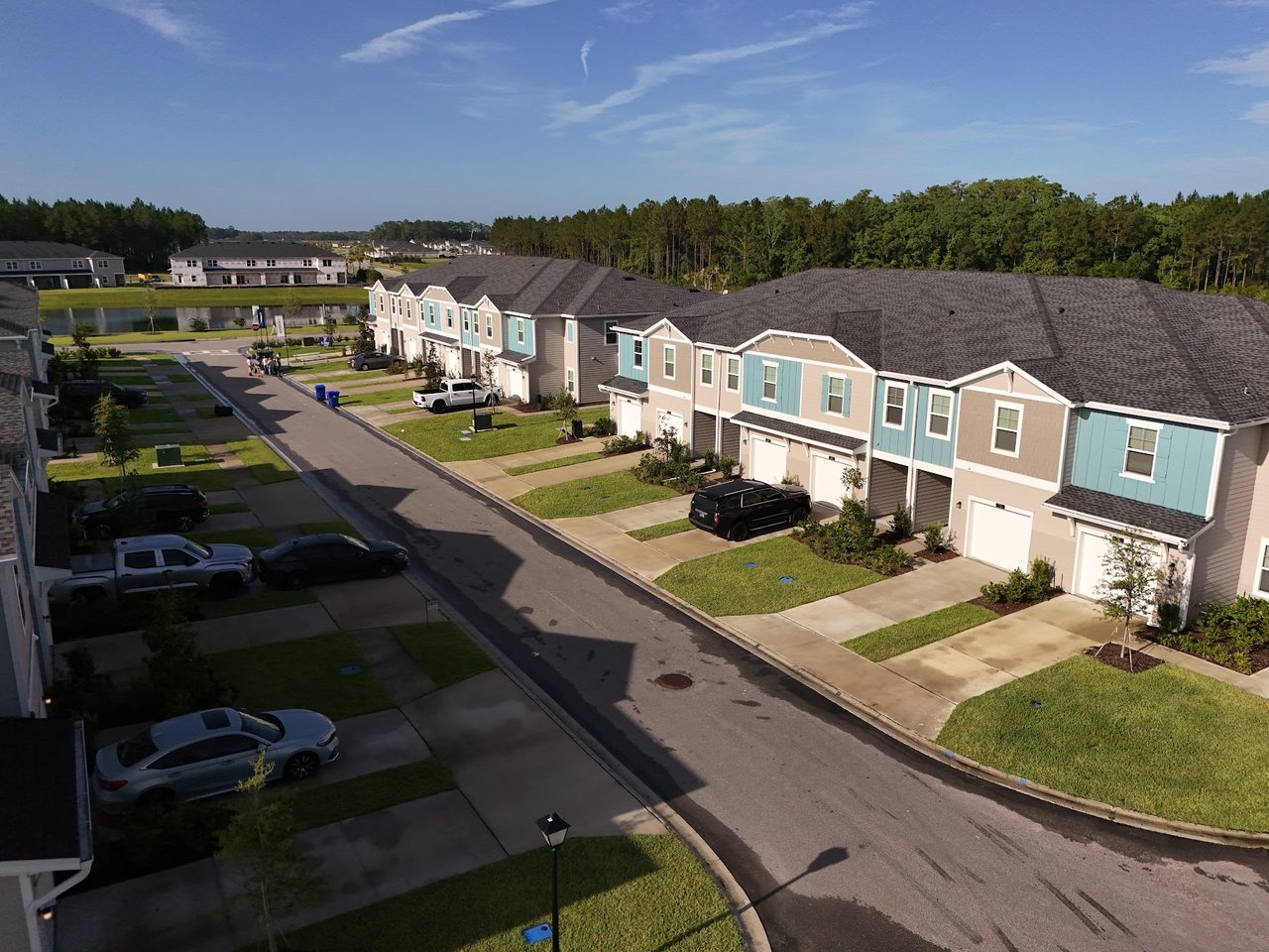 Attached beige and teal townhomes line a residential street with driveways and lawns.