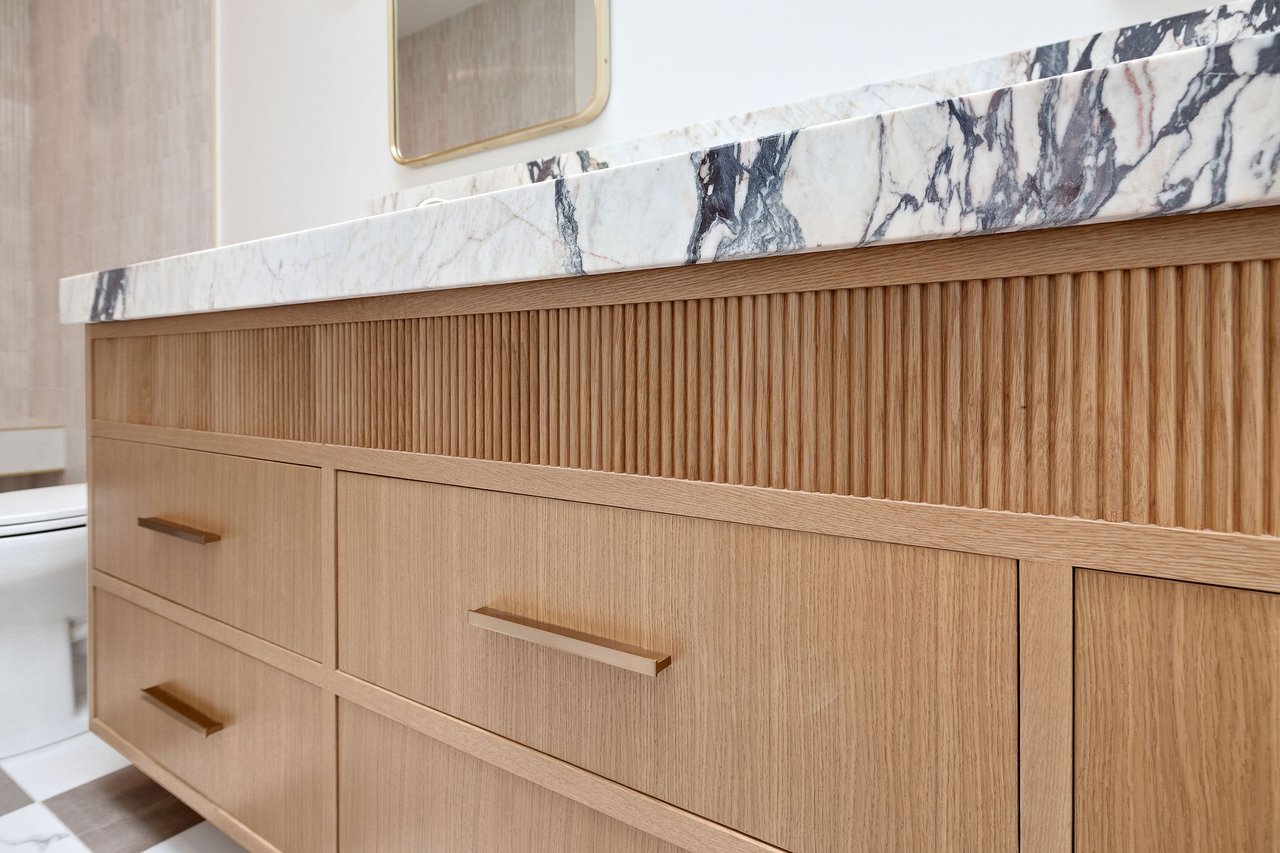 Bathroom vanity with fluted oak cabinetry, brass pulls, and a veined marble countertop.