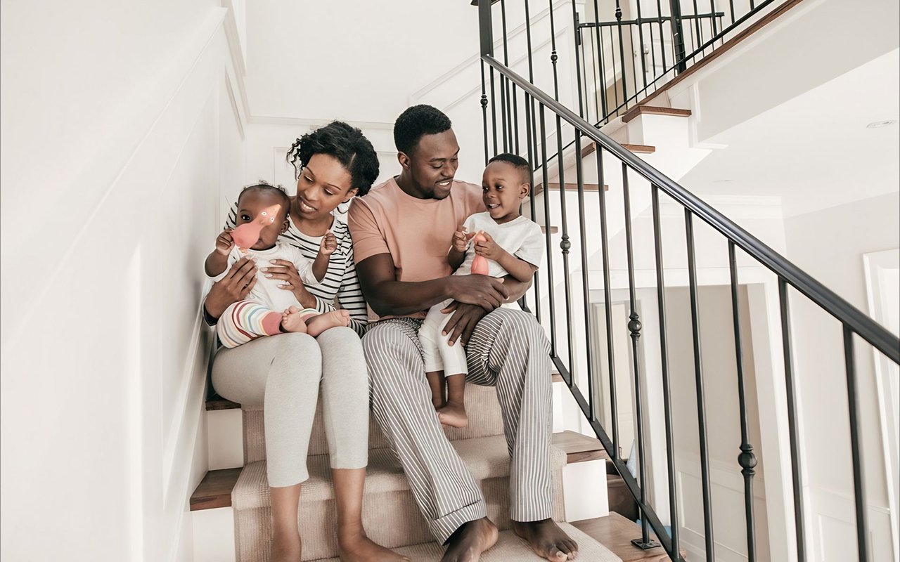 Family of four sitting together on a carpeted staircase in a bright home.