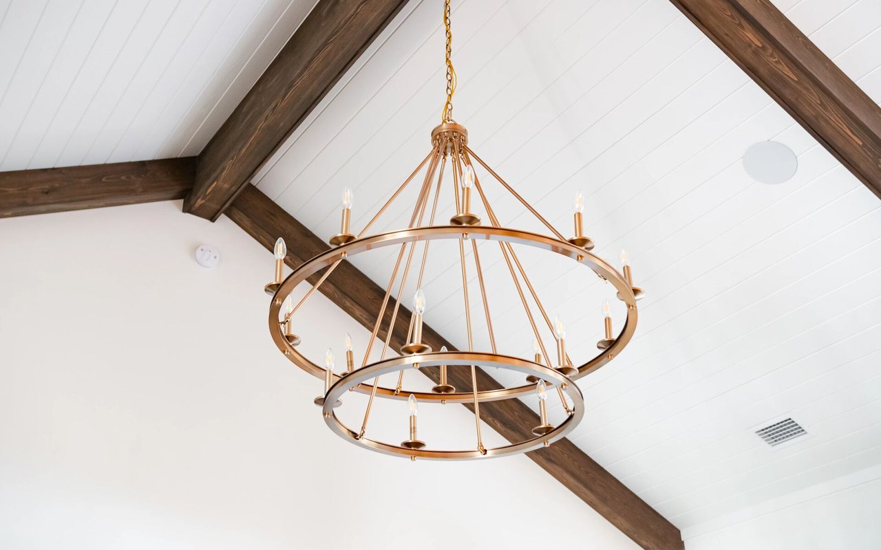 Brass ring chandelier beneath a vaulted white ceiling with dark exposed beams.