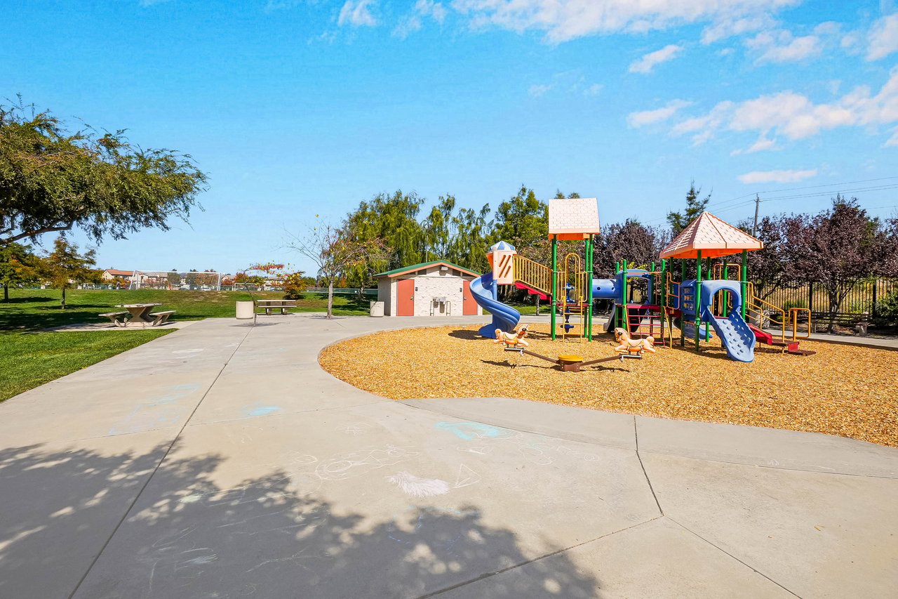 Neighborhood park with colorful playground equipment, chalk drawings on pavement, and picnic tables.
