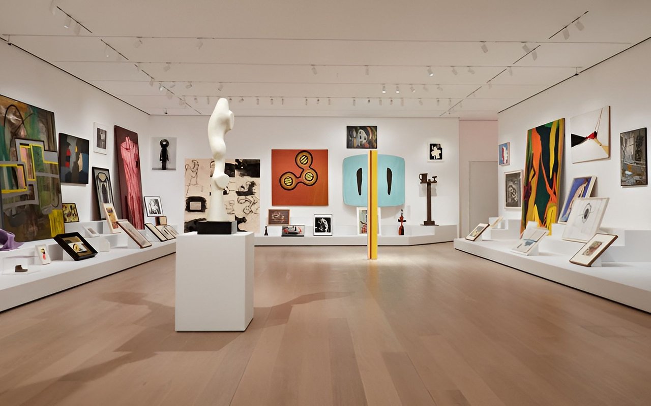 Modern art gallery with paintings and sculptures displayed throughout a bright white room.