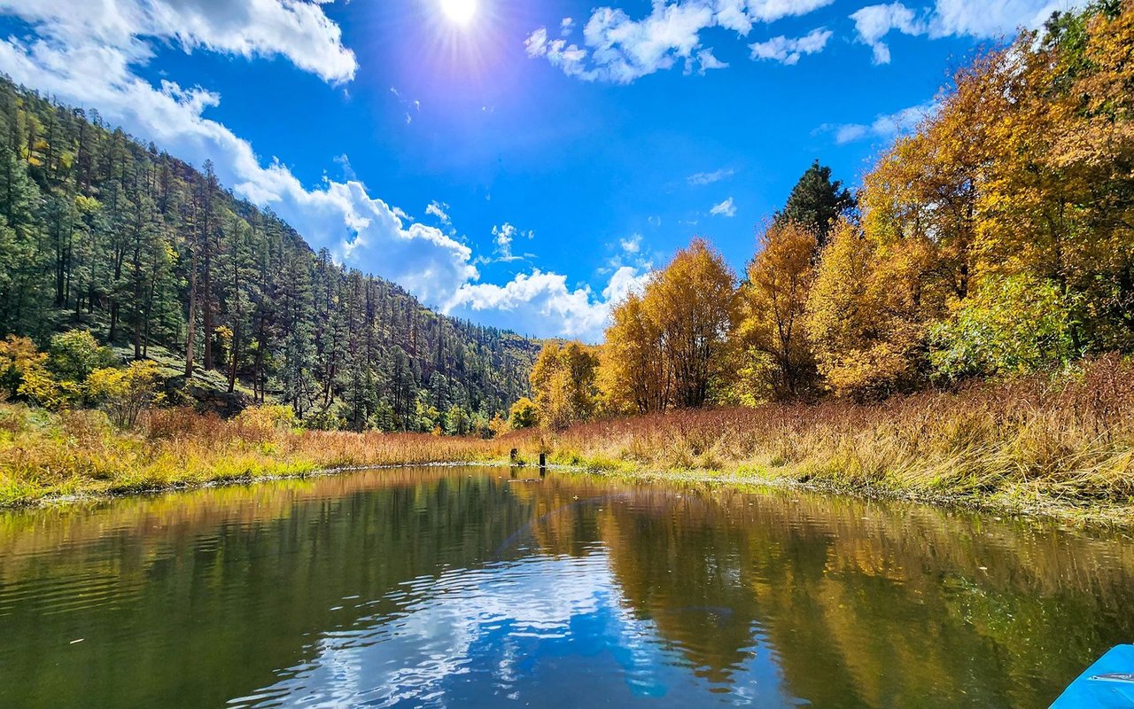 Pond reflecting blue sky beneath autumn-colored trees and forested hills.