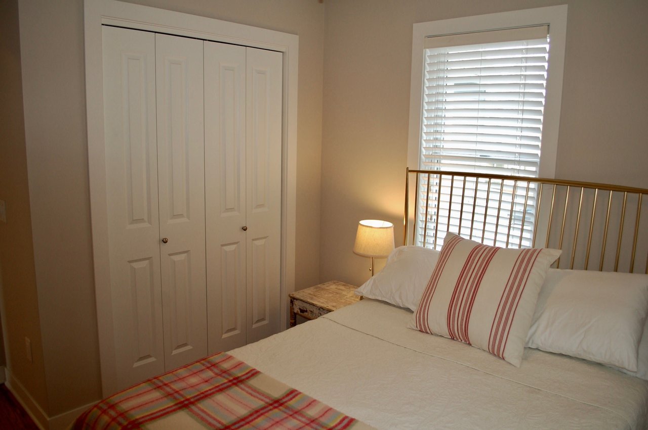 Bedroom with a white bed, striped accents, brass headboard, and window blinds.