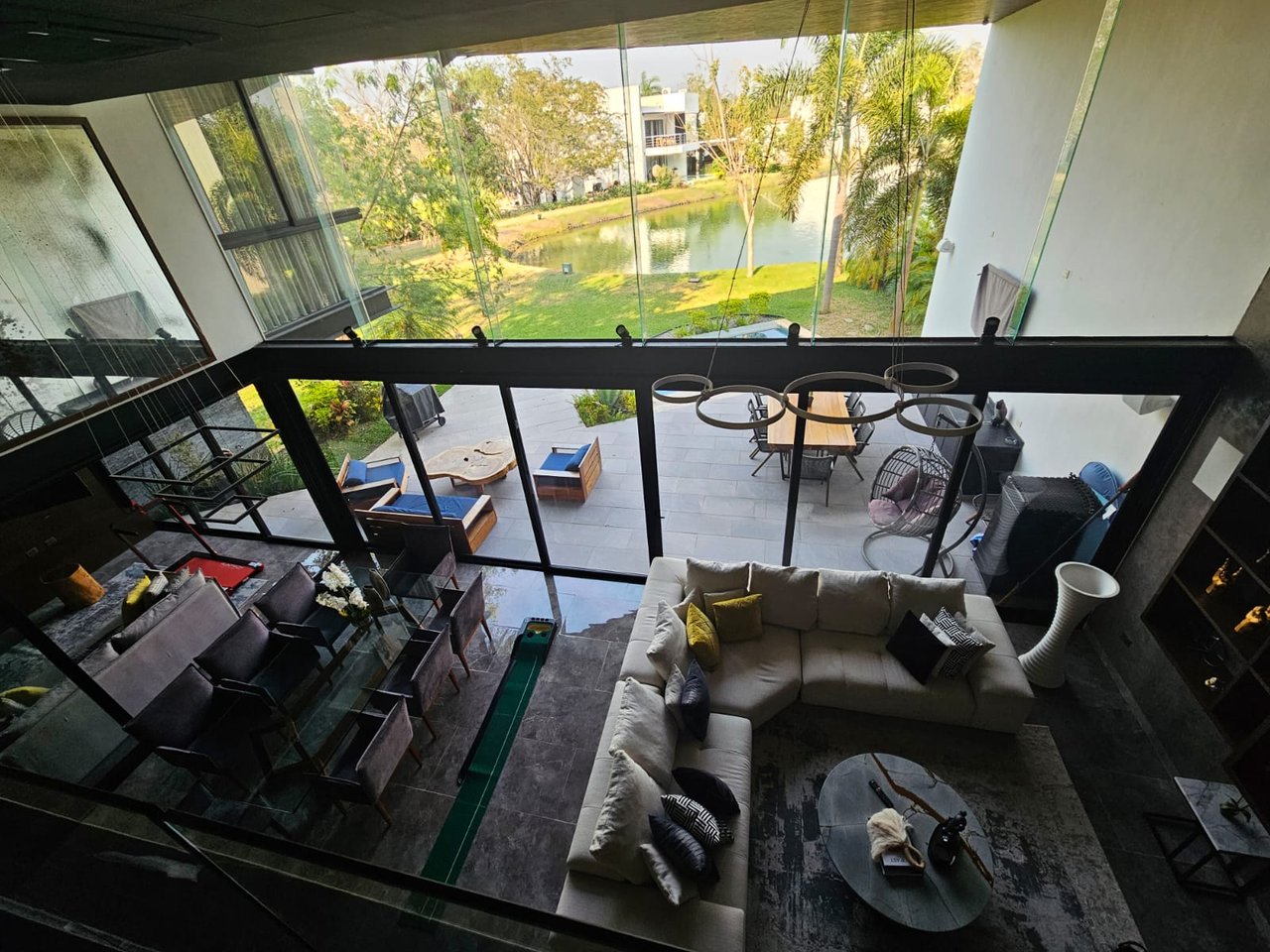 Furnished living room with floor-to-ceiling glass overlooking a patio and pond.