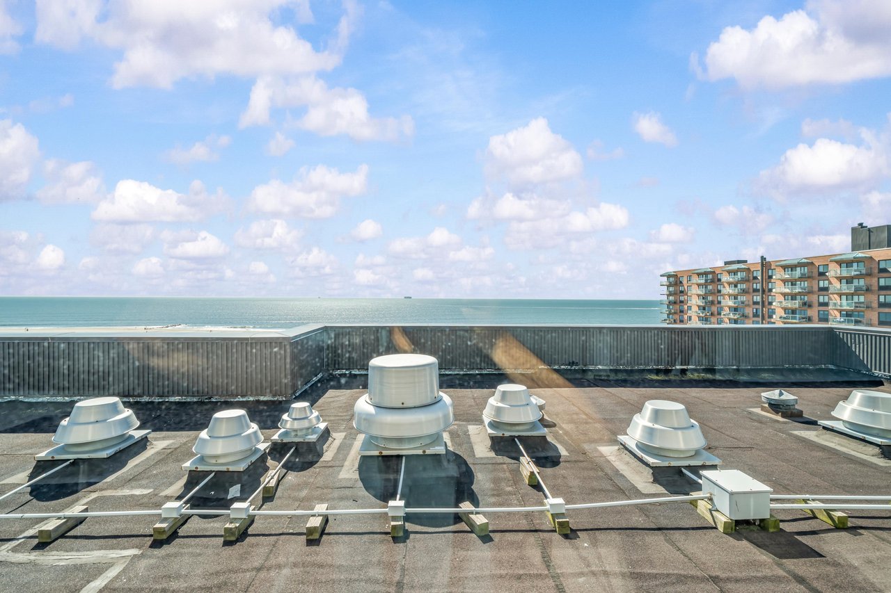 Rooftop with ventilation units overlooking the ocean and a neighboring beachfront apartment building.