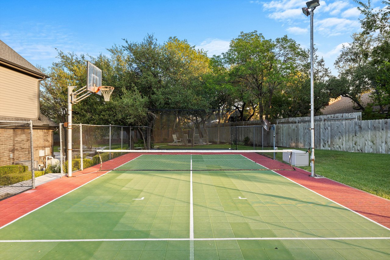 Lighted sport court with paddle tennis net, exterior fans, and sports rebounder