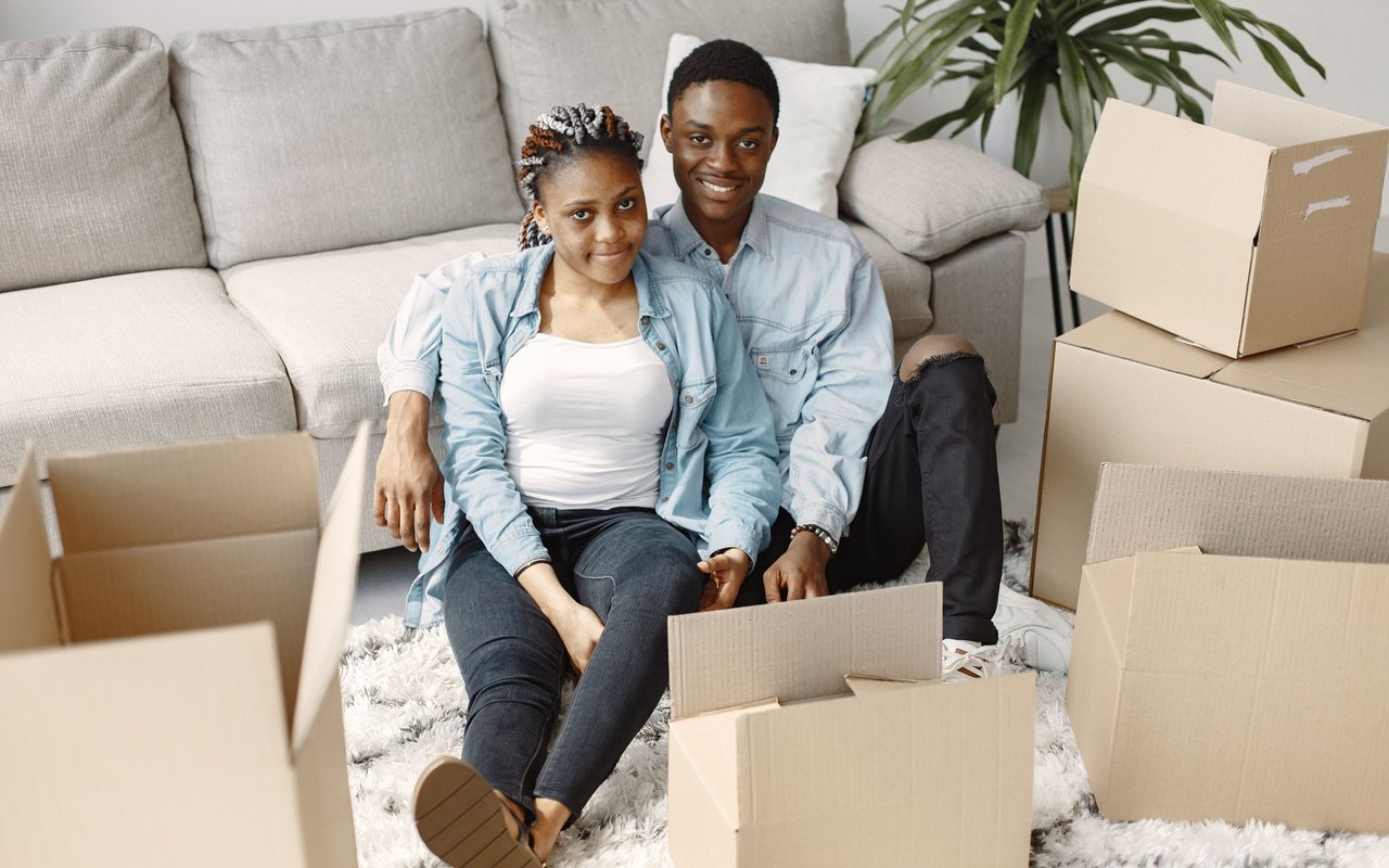 A young couple sits among moving boxes in their living room.