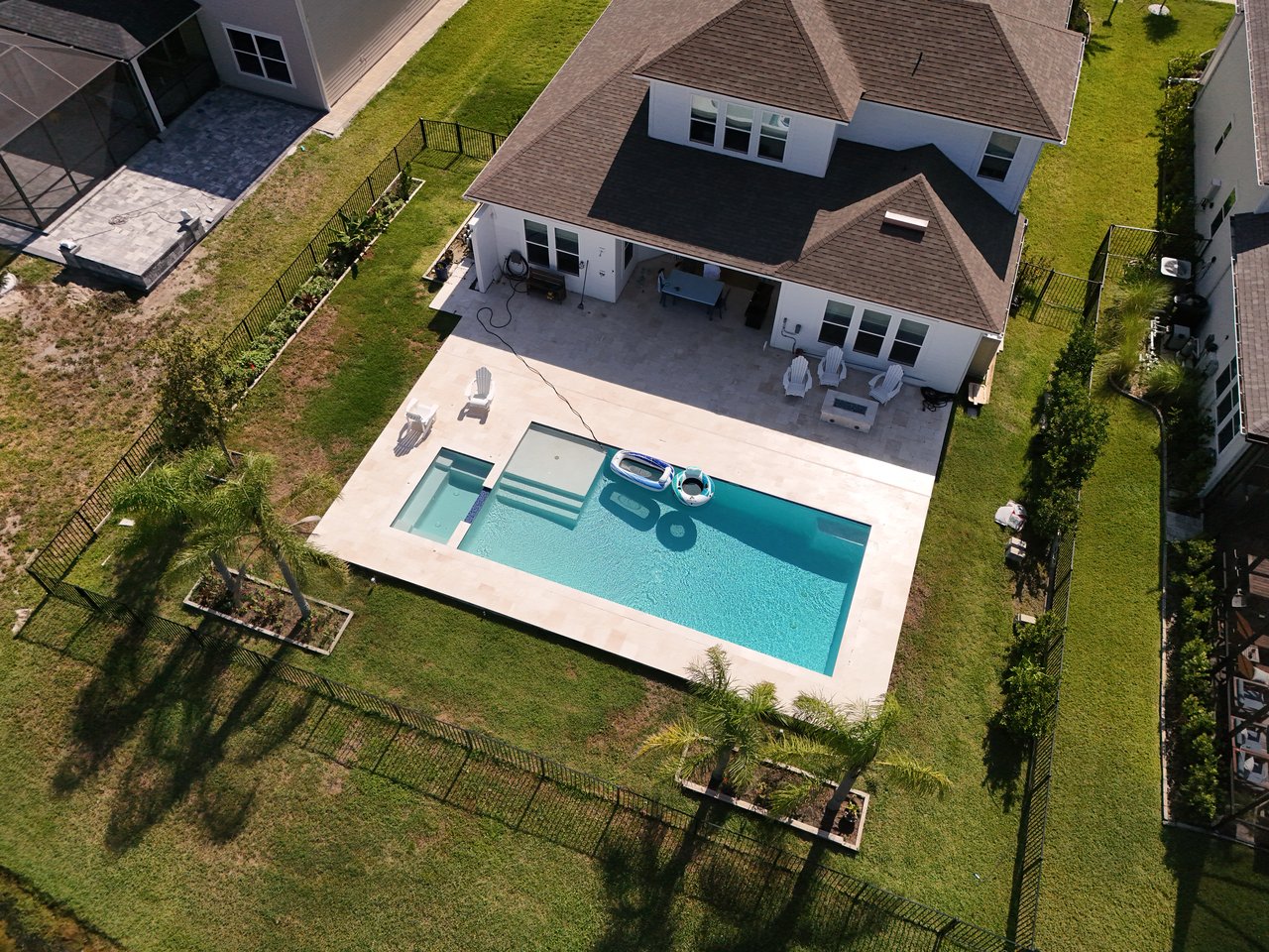 Aerial view of a two-story home with a fenced yard, spacious patio, and rectangular swimming pool.
