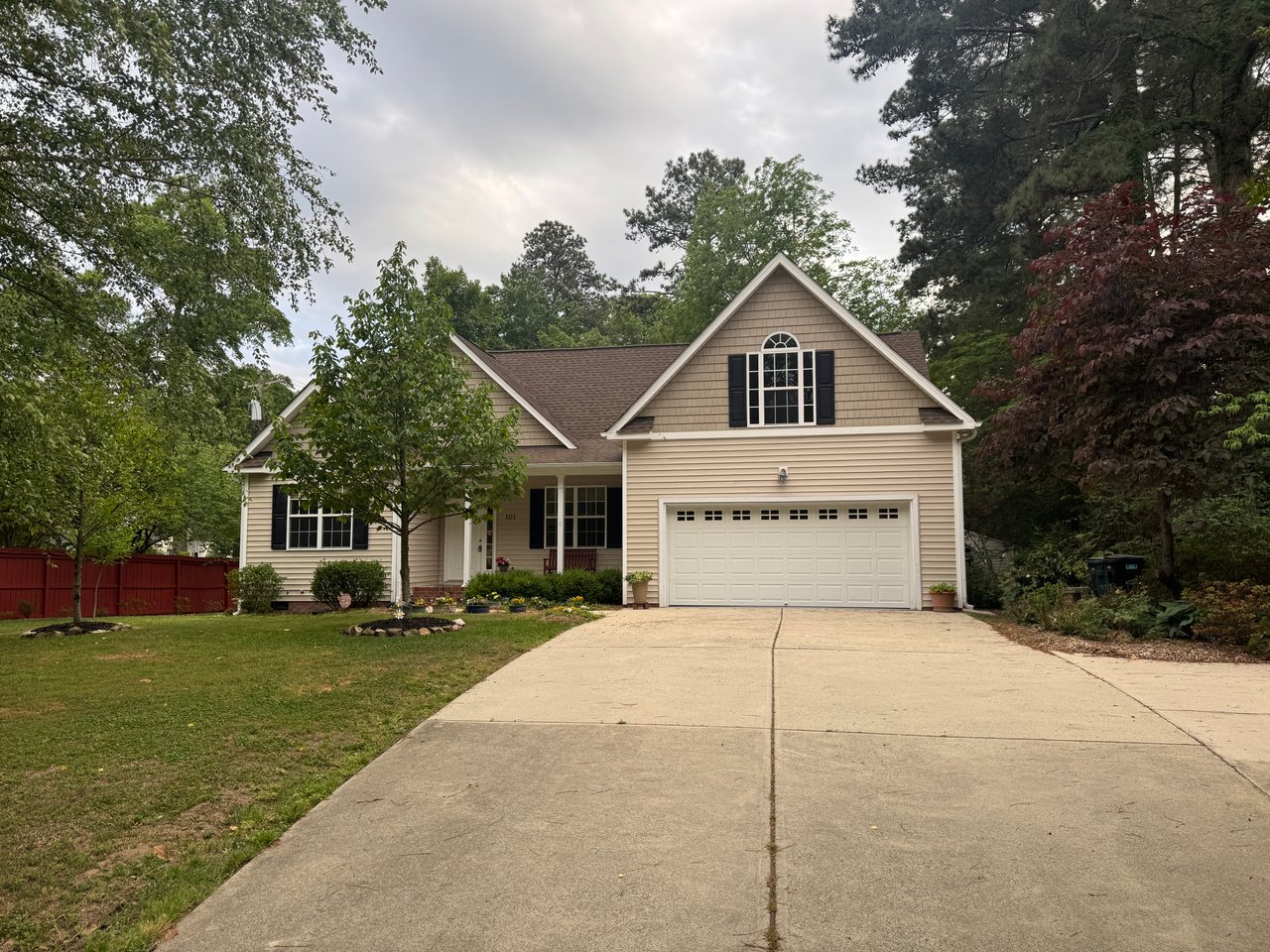 Beige two-story home with a white double garage, broad driveway, and mature trees.