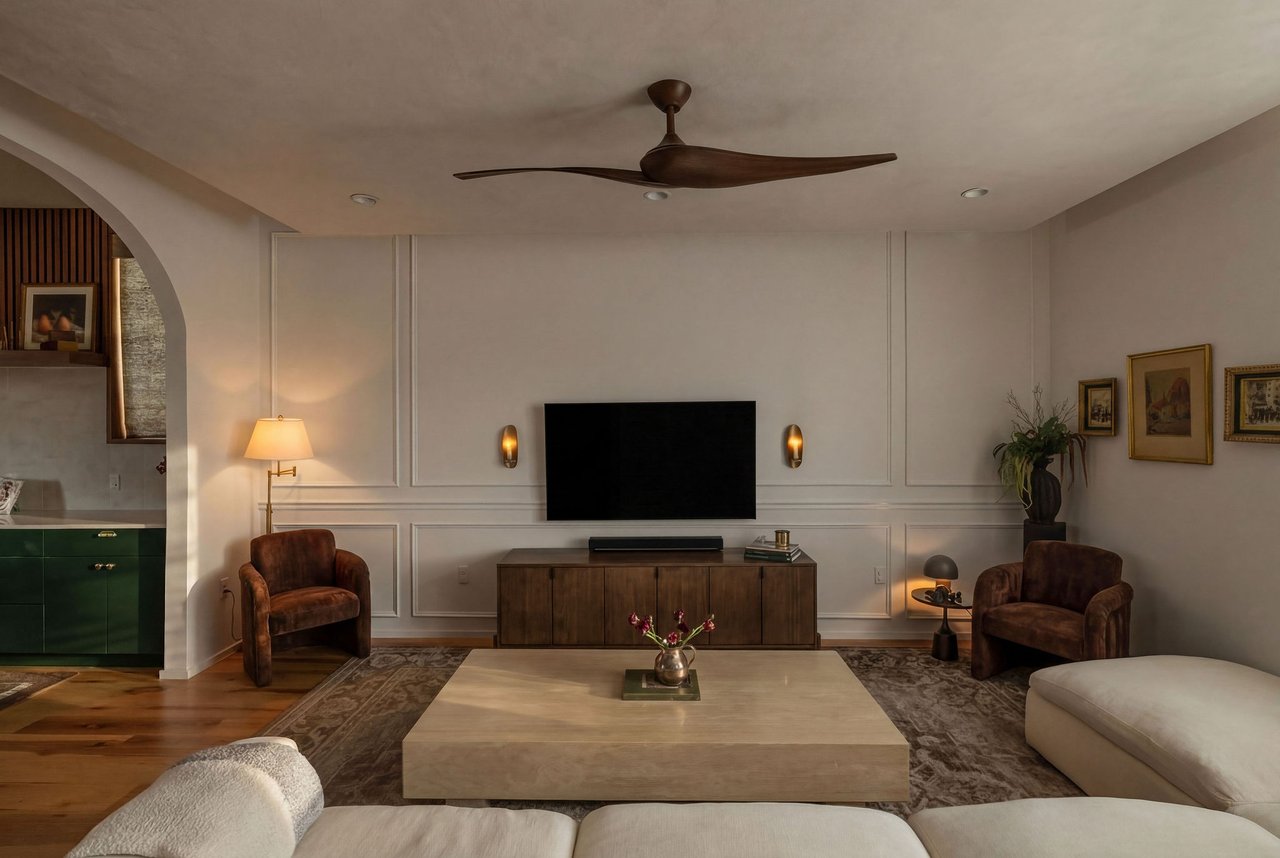 Living room with paneled walls, a wall-mounted TV, brown armchairs, and a pale stone coffee table.