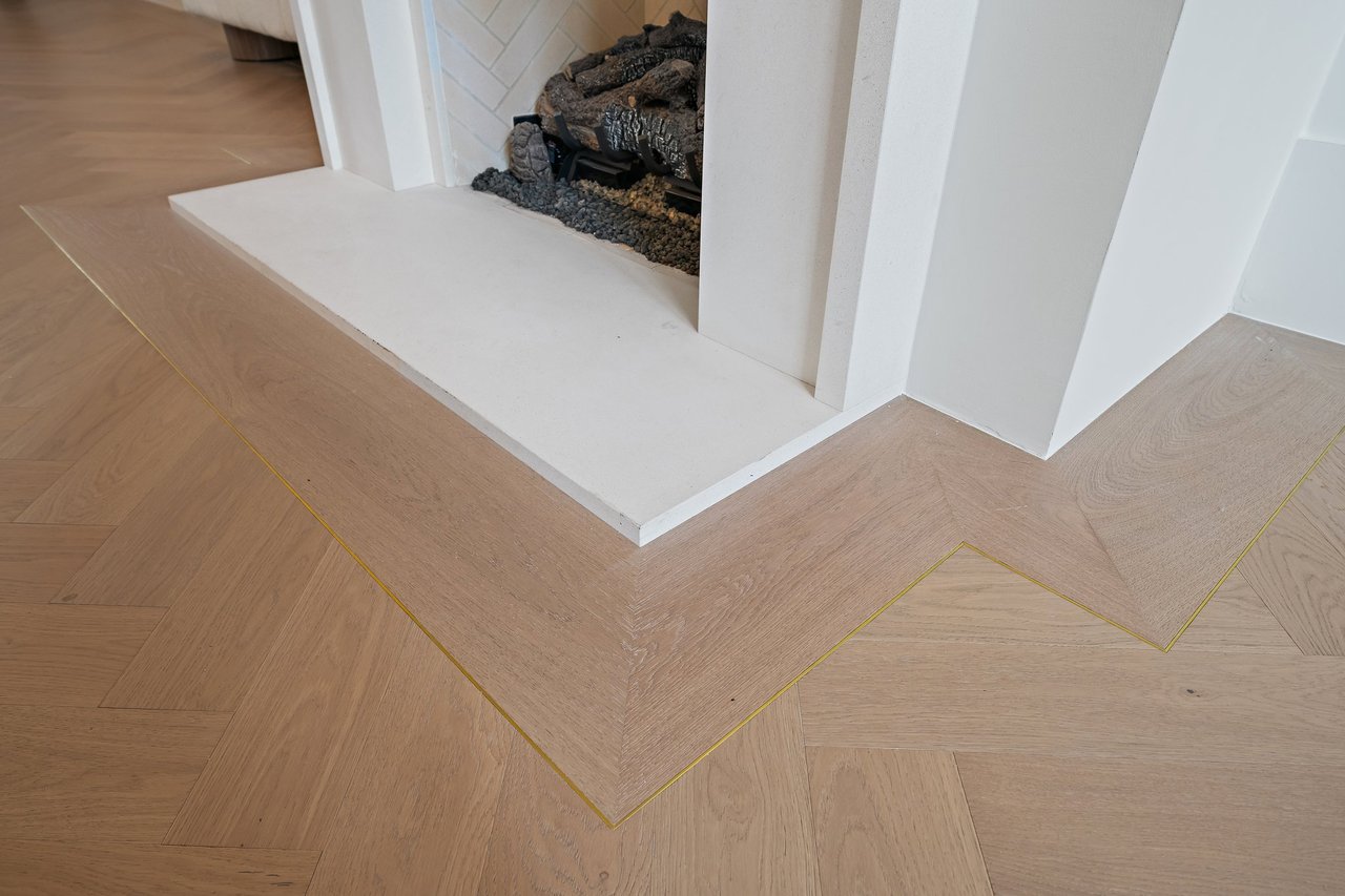 Modern fireplace with a white hearth and surround above oak herringbone flooring with geometric inlay.