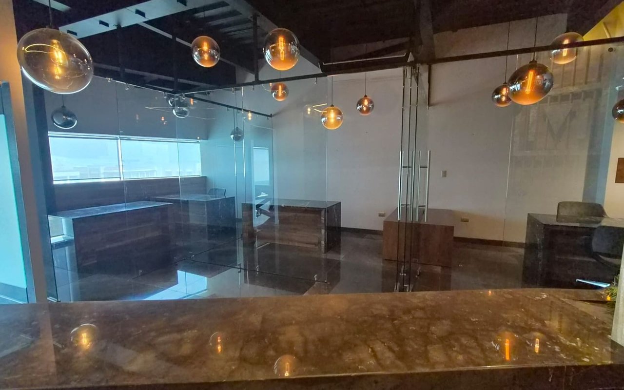Modern office with glass partitions, dark stone counters, and spherical pendant lights.