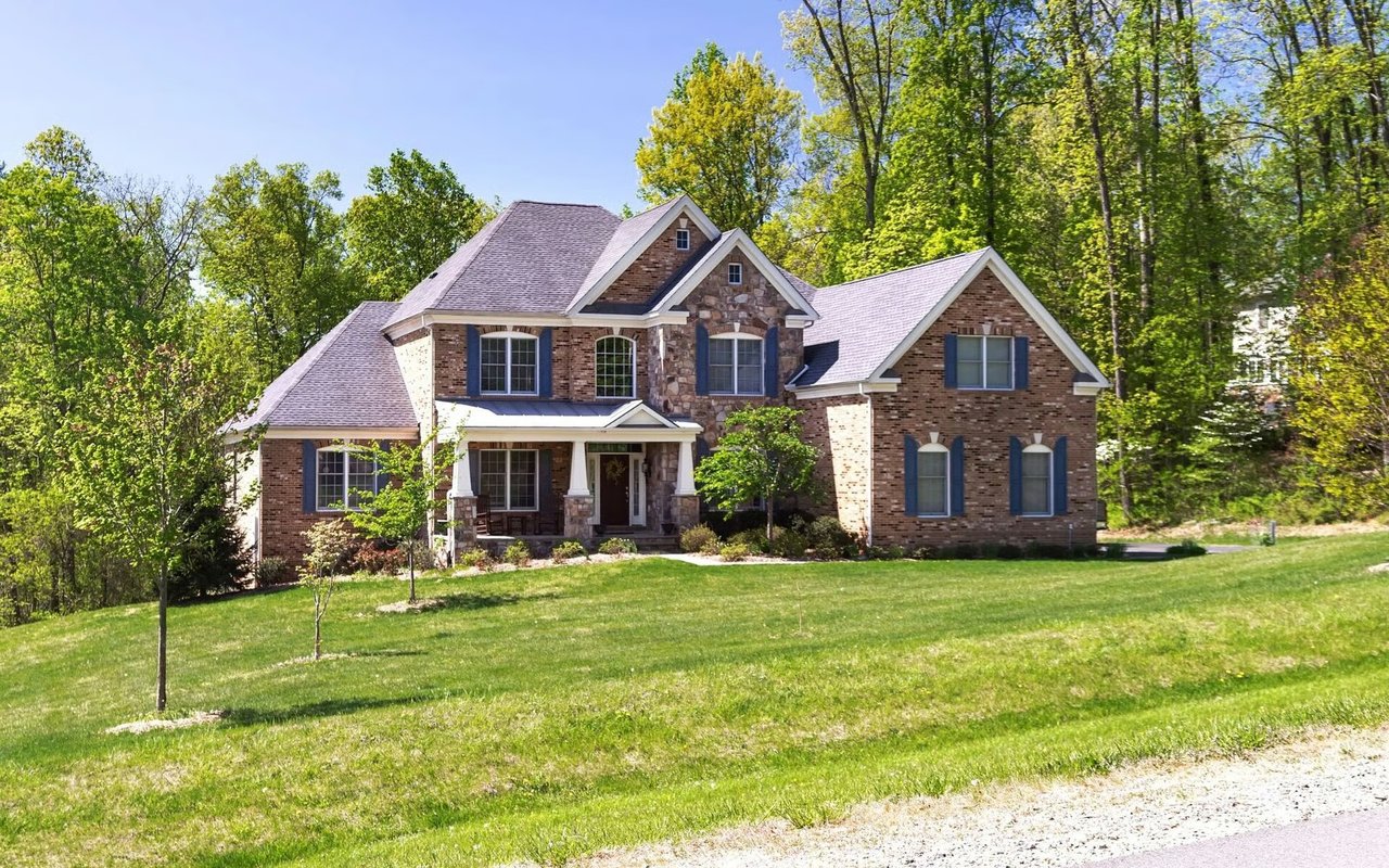 Two-story brick and stone house with a covered porch, blue shutters, and a broad lawn.