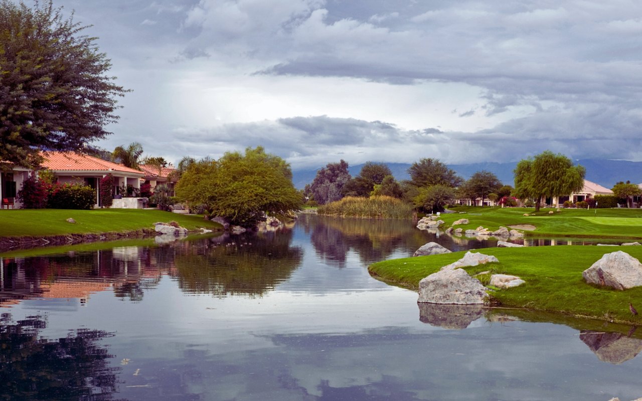 Golf course pond bordered by green fairways, rocks, mature trees, and homes.