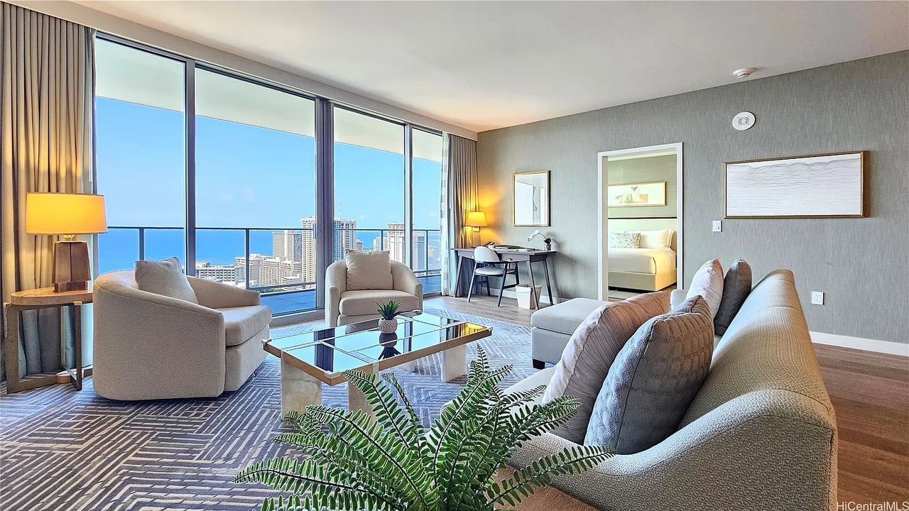Furnished living room with floor-to-ceiling windows overlooking the ocean and city skyline.