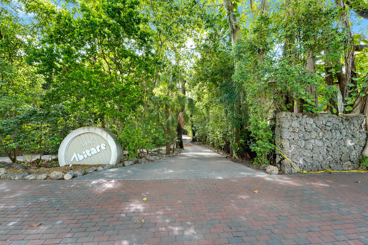 Abitare entrance at 3495, framed by dense tropical greenery and a stone wall.