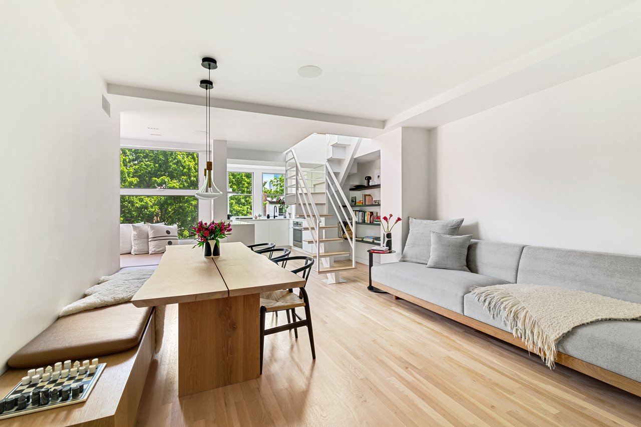 Bright Scandinavian-style open living and dining area featuring light oak flooring, a modern white staircase, and built-in wooden bench seating.