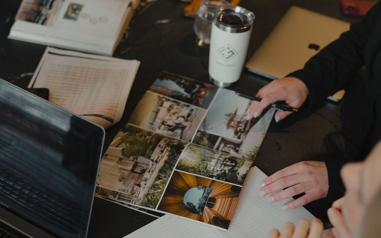 People review property brochures and photos around a table beside a laptop and notebook.