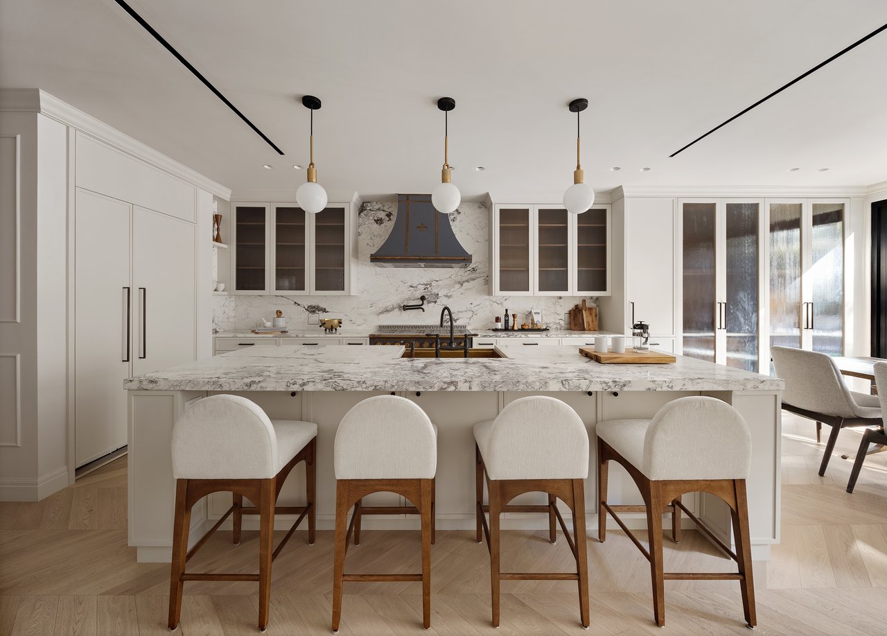 Kitchen with a marble island, four upholstered stools, white cabinetry, and three pendant lights.
