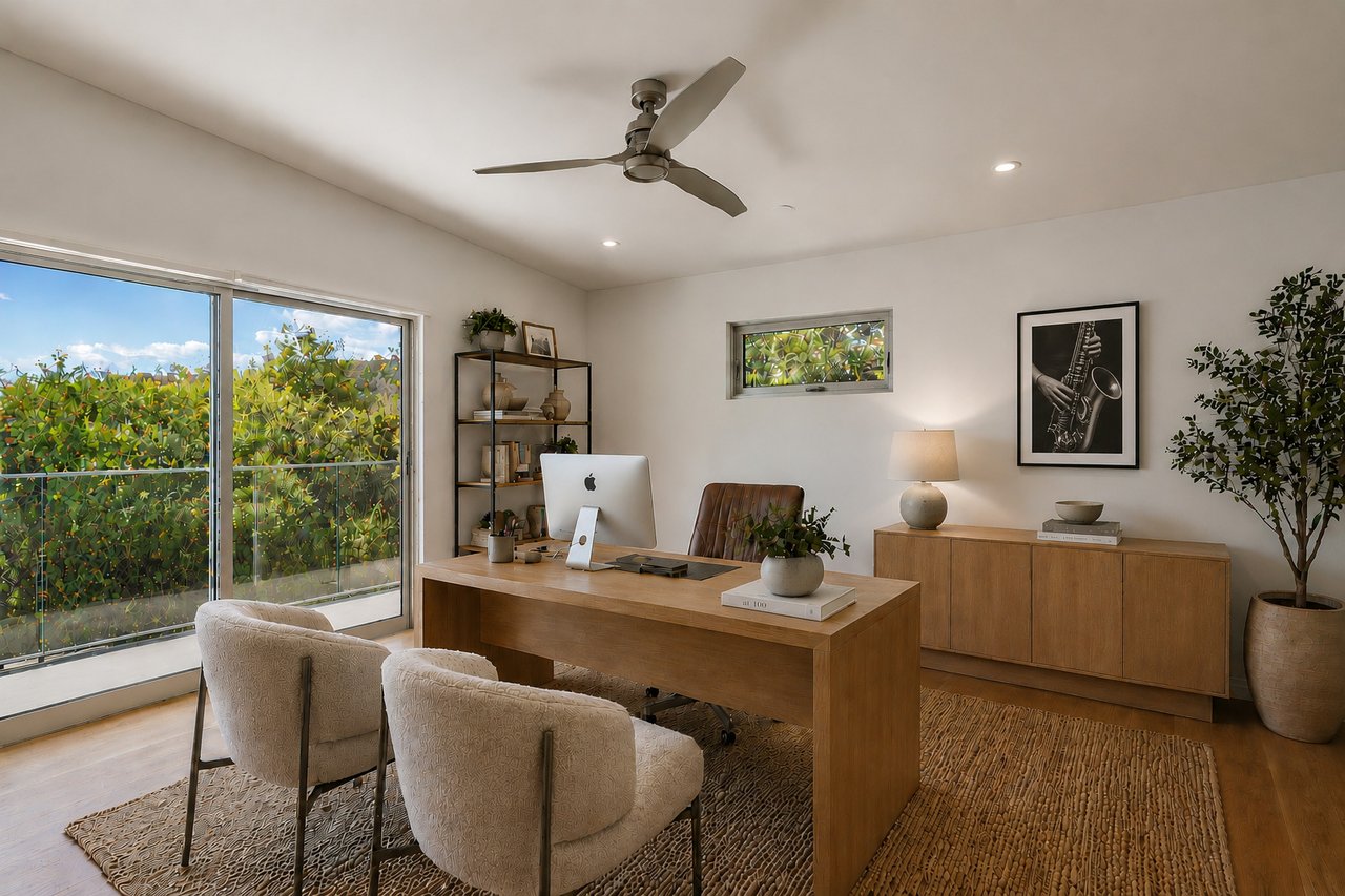 Furnished home office with a wood desk, guest chairs, and sliding glass doors overlooking greenery.