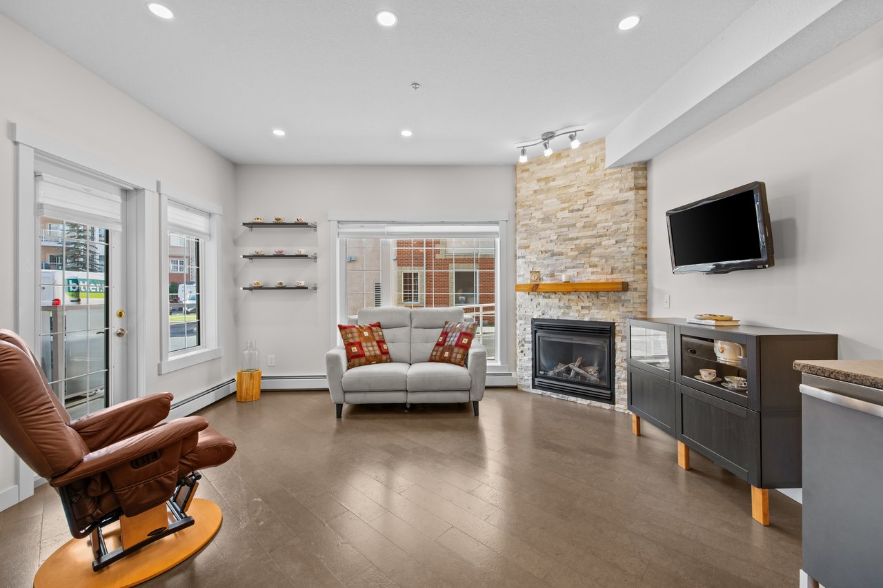 Living room with a stone fireplace, gray loveseat, leather recliner, and large windows.